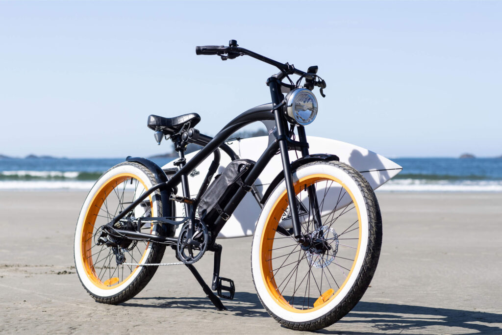 Detailaufnahme eines schwarzen E-Bikes am Strand mit dem Namen MB Vacay Gentleman bei MC E-Bike, hoher Einstieg, schwarzer Rahmen, schwarzer Sattel und schwarze Griffe, Weißwand-Fatbike-Reifen, 26 Zoll