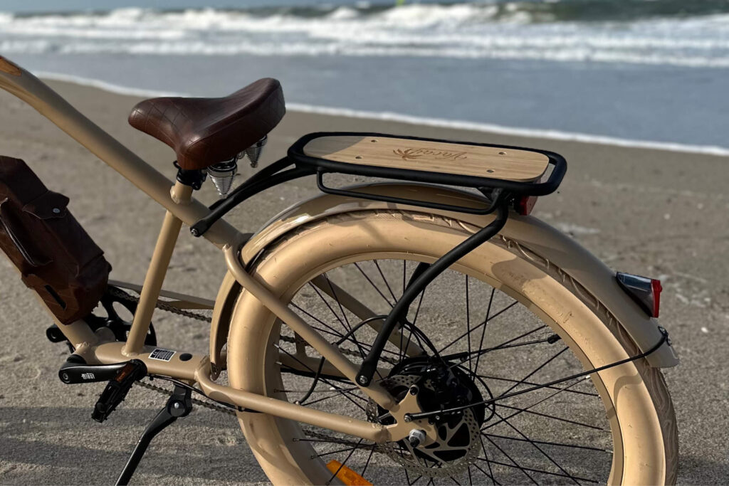 Detailaufnahme eines schwarzen E-Bikes am Strand mit dem Namen MB Vacay Gentleman bei MC E-Bike, hoher Einstieg, schwarzer Rahmen, schwarzer Sattel und schwarze Griffe, Weißwand-Fatbike-Reifen, 26 Zoll, , Aufnahme des Gepäckträgers am hinteren Teil des Rads