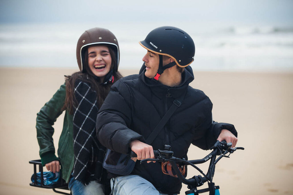 Aufnahme zweier Personen auf einem schwarzen E-Bikes mit dem Namen MB Ponyboy, schwarzer Rahmen, schwarzer langgezogener Sitz und schwarze Griffe, schwarze Fatbike-Reifen, 20 Zoll
